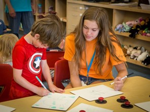 A high school student smiling while helping kids with their homework. A high school student smiling while helping kids with their homework.